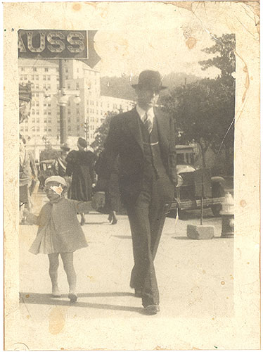 This is a snapshot of a young girl and her father walking in downtown Hot Springs, Arkansas sometime in the 1930s. Carol removed splotches, scratches, and stains, improved the contrast and sharpened the image. She also painted in the missing portion of the child's face.